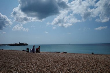 İnsanlar mavi gökyüzü olan bir plajda oturuyor.