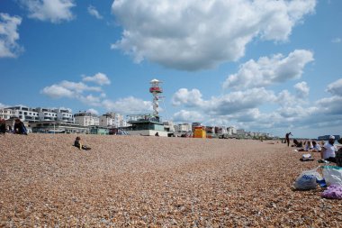 Kumsalda insanların oturduğu ve gökyüzünde uçan bir uçurtma.