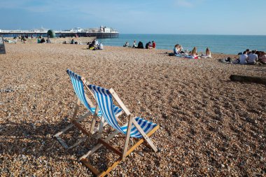 Birkaç sandalyesi olan bir plaj ve kumsalda oturan insanlar.