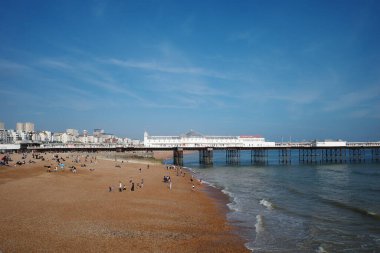 İnsanların yürüdüğü bir sahil ve arka planda bir rıhtım.