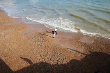 Okyanus kıyısındaki bir sahilde yürüyen iki kişi.