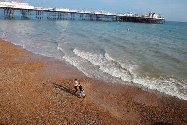 Okyanus kıyısındaki bir sahilde yürüyen iki kişi.