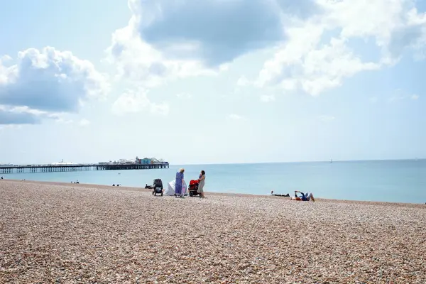 Kumsalda insanların oturduğu ve arka planda bir iskelenin olduğu bir kumsal.