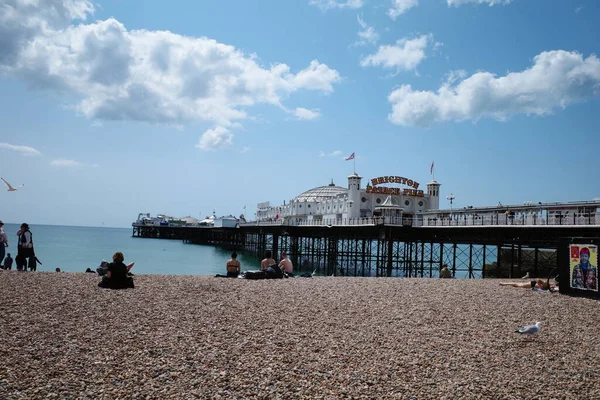 Kumsalda insanların oturduğu ve arka planda bir iskelenin olduğu bir kumsal.
