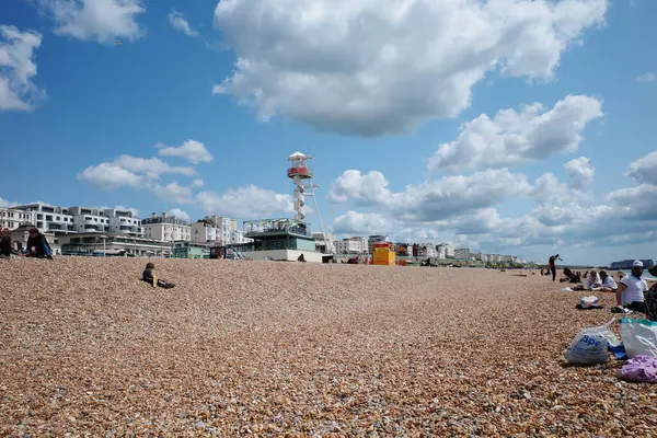 Kumsalda insanların oturduğu ve gökyüzünde uçan bir uçurtma.