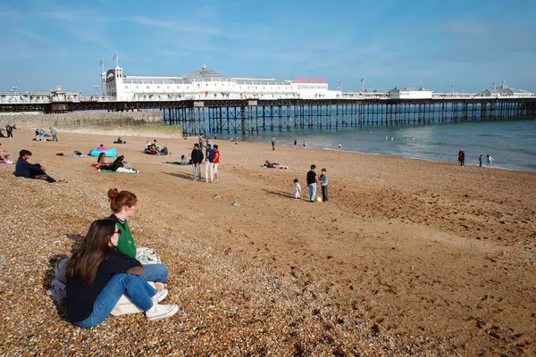 Kumsalda insanların oturduğu ve arka planda bir iskelenin olduğu bir kumsal.