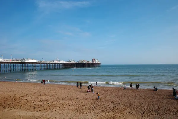 İnsanların yürüdüğü bir sahil ve arka planda bir rıhtım.