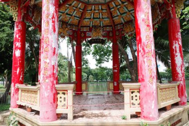 Arka planda gölcük olan kırmızı ve beyaz bir çardak.