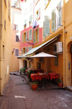 Masaları, sandalyeleri ve şemsiyeleri olan dar bir sokak.