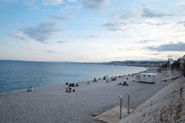 Kumda yürüyen ve oturan insanların olduğu bir sahil.