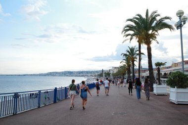 Bir grup insan okyanusun kıyısında bir kaldırımda yürüyor.