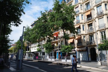 Uzun bir binanın önündeki caddede yürüyen bir adam.