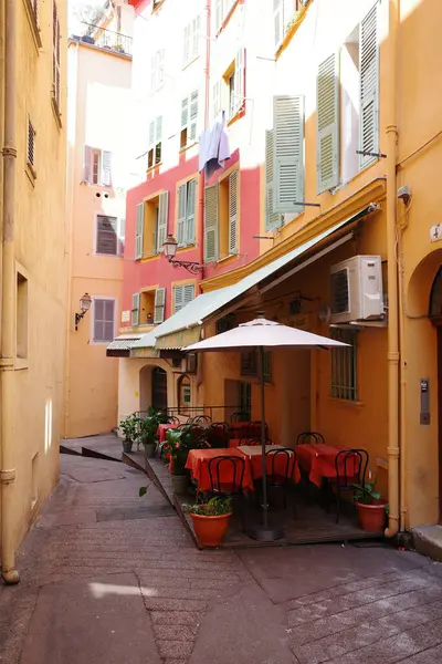 Masaları, sandalyeleri ve şemsiyeleri olan dar bir sokak.