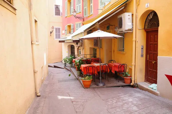 Masaları, sandalyeleri ve şemsiyesi olan dar bir sokak.