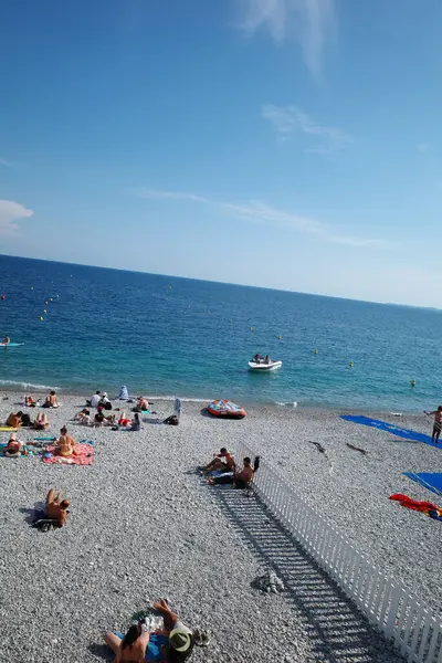 Kumsalda insanların yattığı ve suda bir teknenin olduğu bir kumsal.