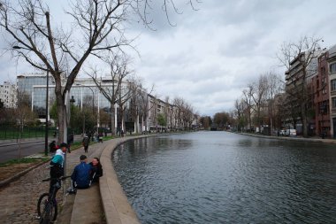 Nehrin kıyısındaki bankta oturan iki kişi.