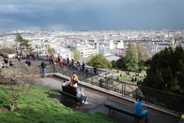 Bir grup insan şehre tepeden bakan bir bankta oturuyor.