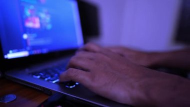 Renkli içeriği gösteren bulanık bir ekranla dizüstü bilgisayarda yazı yazan ellerin yakın çekimi. Sahne mavi bir tonla aydınlatılmış. Teknoloji odaklı bir ortam yaratıyor..