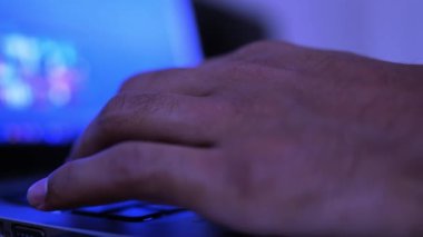 Bir insanın dizüstü bilgisayarda arka planda mavi bir ekranla yazarken yakın plan görüntüsü..