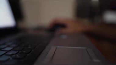 Fare kullanan bir eli gösteren bulanık arka planı olan bir dizüstü bilgisayarın yakın plan görüntüsü..