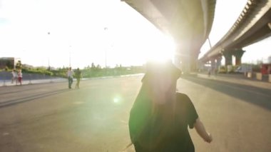 Uzun düz saçlı, parlak güneş ışığında köprünün altında dans eden etkileyici bir genç kadın. Orta çekim