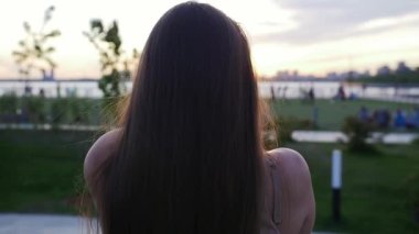 Gün batımında parkta yürüyen ve kameraya doğru dönen güzel, uzun düz saçlı bir kadın. Portre