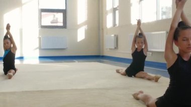 Bir grup plastik kız jimnastikçi spor salonunda egzersiz yapıyor. Orta çekim