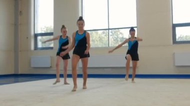 Üç jimnastikçi kız dans salonunda performanslarını sergiliyor. Orta çekim