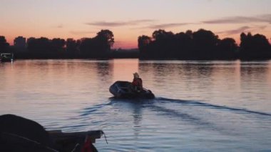Baba ve oğul, pembe bir günbatımında şişme bir tekneyle uzaklara yelken açarlar. Orta çekim