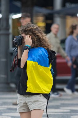 10-29-2022 LISBON, PORTUGAL: Lizbon 'daki Ukrayna protestosu - boynundaki Ukrayna bayrağı ile bağlanmış bir kadın kamera önünde toplantının fotoğraflarını çekiyor. Orta çekim