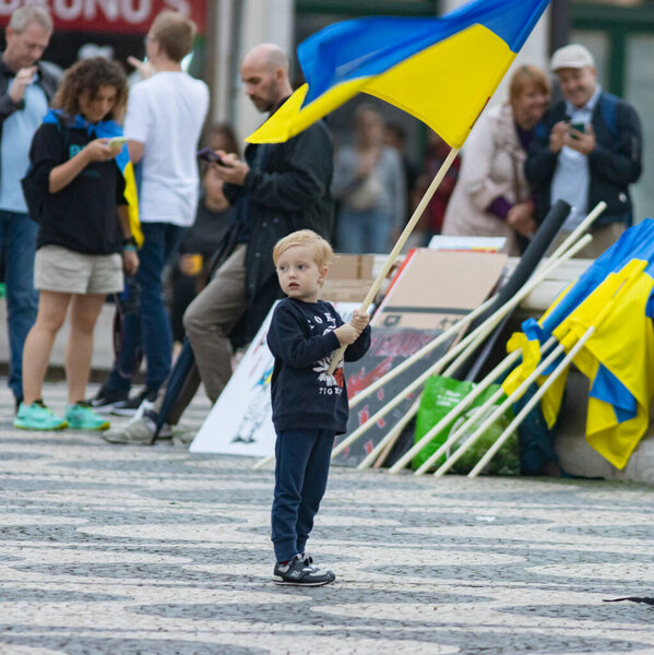 10-29-2022 ЛИСБОН, ПОРТУГАЛЬ: Украинский протест в Лиссабоне - маленький мальчик держит украинский флаг на площади во время протеста. Средний выстрел
