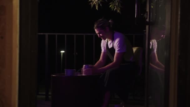 一个面带微笑的年轻人晚上在阳台上练习陶器 — 图库视频影像
