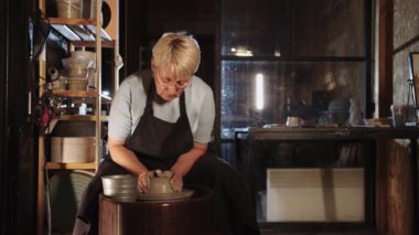 Yaşlı bir çömlekçi kadın bir atölyede kille çalışıyor. Orta çekim