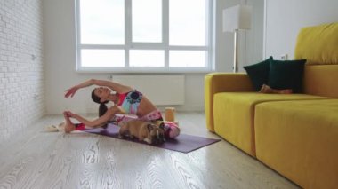 Yoga minderinin üzerinde evcil köpeğinin yanında egzersiz yapan bir kadın. Orta çekim