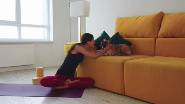 Mujer Delgada Sentada Una Esterilla Yoga Junto Sofá Amarillo Acariciando — Vídeos de Stock