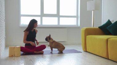 Zayıf bir kadın yoga minderinde oturup evcil köpekle oynuyor. Orta çekim