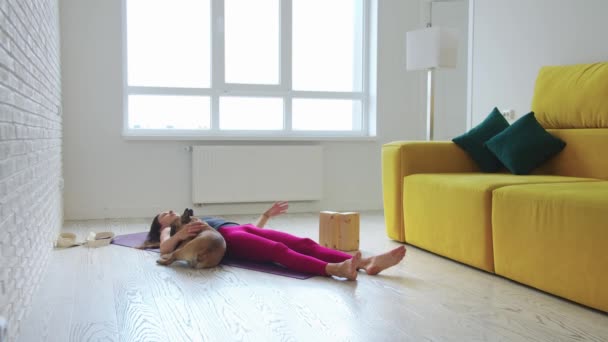 一个瘦小的女人躺在瑜伽垫上 她的宠物狗走近她 向她求爱 — 图库视频影像