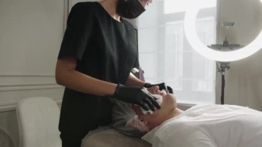Güzellik tedavileri. Kadın kozmetikçi, erkek müşterinin yüzünü pamuk pedlerle siliyor. Orta çekim