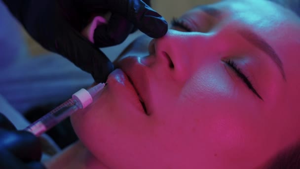 リップ充填手順 ネオン照明にきれいな女性クライアントの下唇に針を挿入します ミッドショット — ストック動画