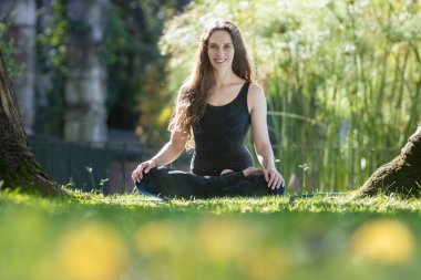 Nilüfer pozisyonunda yoga minderinde oturan ve kameraya bakan gülümseyen kadın. Orta çekim
