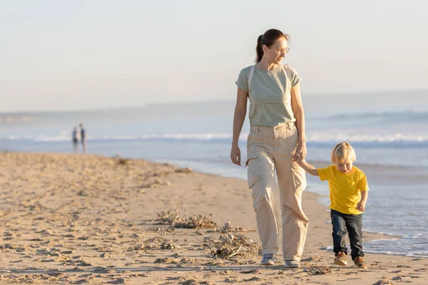 一个金发碧眼的小男孩和他的妈妈在海边散步 — 图库照片