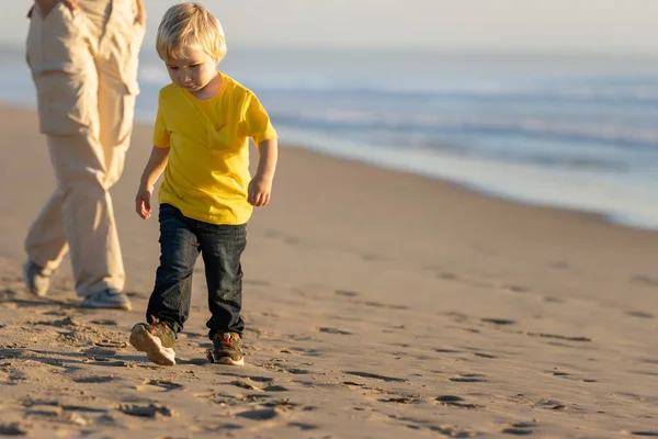 一个金发碧眼的小男孩和他的妈妈在海边散步 — 图库照片