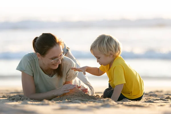 一个金发碧眼的小男孩和他的妈妈在海滩上玩沙子 — 图库照片