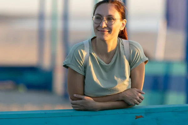 stock image Ginger woman in glasses stands in the port and leans her forearms into blue planks. Mid shot