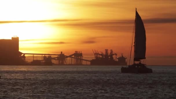 Barcos Vela Rio Durante Pôr Sol Laranja Guindastes Industriais Fundo — Vídeo de Stock