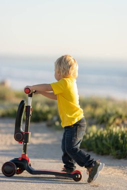 Gülümseyen sarışın çocuk scooter 'da kayıyor. Dikey çekim