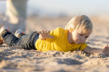 Sarışın küçük çocuk kumların üzerinde yatıyor. Orta çekim