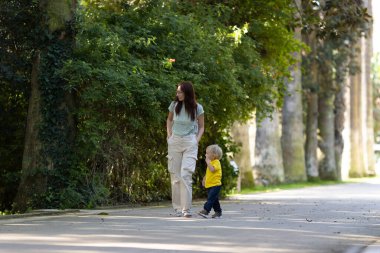 Küçük sarışın oğluyla parkta yürüyen bir kadın. Orta çekim