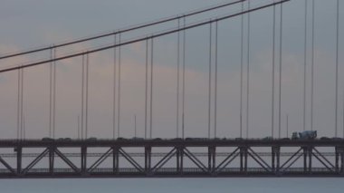 Araç, bulutların arka planına karşı asma bir köprüde ilerliyor. Orta çekim