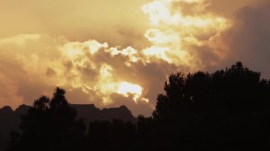Gökyüzünde süzülen bulutlar ve köyün üzerindeki bulutları aşan güneş. Orta çekim